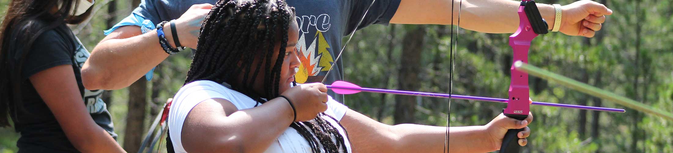 Young girl with bow and arrow performing archery at The Salvation Army High Peak Camp Colorado